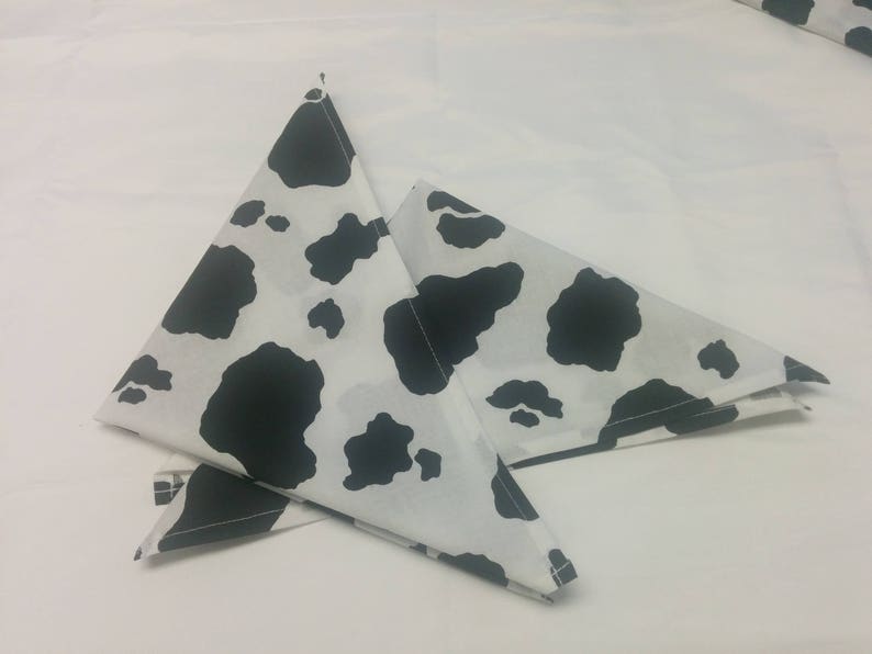 May include: Two black and white cow print fabric triangles folded in half. The fabric is white with black spots.