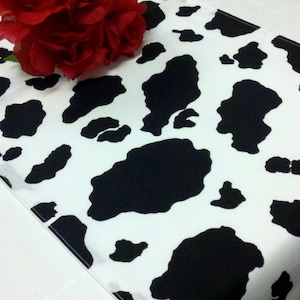 May include: A white table runner with a black and white cow print pattern.