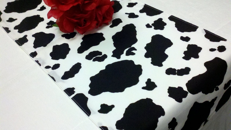 May include: A white table runner with a black and white cow print pattern.