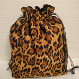 May include: A leopard print drawstring bag with black ribbon ties. The bag is made of a soft, brown fabric with a leopard print pattern.