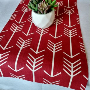 May include: Red table runner with a white arrow pattern. The runner is decorated with a small potted succulent plant.
