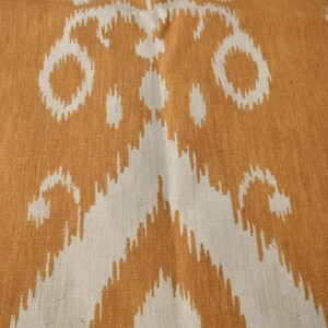 May include: Close-up of a textile with a repeating pattern in shades of orange and white. The design features abstract shapes and lines, creating a textured appearance. The fabric appears to be woven, with visible threads and a slightly rough surface.