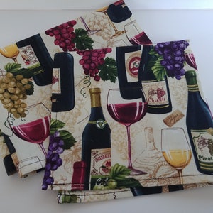 May include: Two white cotton tea towels with a wine theme. The towels feature a repeating pattern of wine bottles, glasses, grapes, and the words "Chianti" and "Pinot Noir".