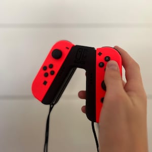 May include: A pair of red and black Nintendo Switch Joy-Con controllers. The left controller has a directional pad and buttons, while the right has action buttons. A black strap is attached to each controller.