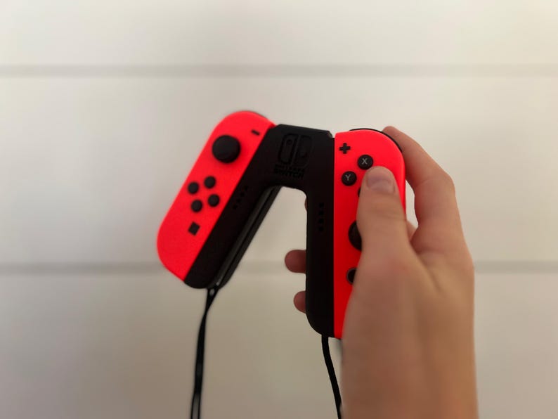 May include: A pair of red and black Nintendo Switch Joy-Con controllers. The left controller has a directional pad and buttons, while the right has action buttons. A black strap is attached to the bottom of each controller.