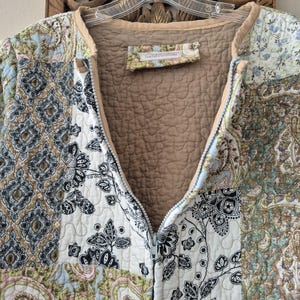 Pu&ograve; includere: Una giacca trapuntata con cerniera caratterizzata da un design patchwork con vari motivi floreali e paisley nelle tonalit&agrave; del blu, verde, nero e bianco. La fodera interna &egrave; color marrone chiaro e sull'orlo del collo &egrave; cucita un'etichetta con la scritta JenTel Creations.