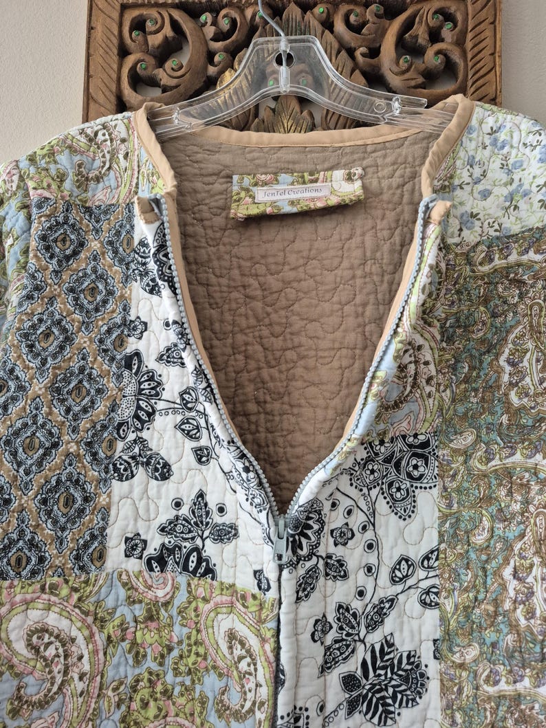 Pu&ograve; includere: Una giacca trapuntata con cerniera caratterizzata da un design patchwork con vari motivi floreali e paisley nelle tonalit&agrave; del blu, verde, nero e bianco. La fodera interna &egrave; color marrone chiaro e sull'orlo del collo &egrave; cucita un'etichetta con la scritta JenTel Creations.