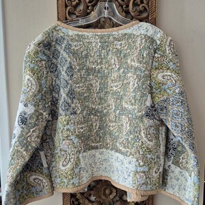 Pu&ograve; includere: Una giacca trapuntata con un design patchwork caratterizzato da vari motivi paisley e floreali nelle tonalit&agrave; dell'azzurro, verde salvia, crema e nero. Il capo presenta maniche lunghe, scollo rotondo e un bordo in tinta unita beige.
