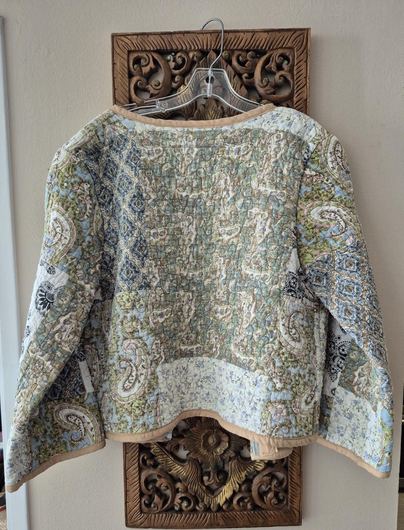 Pu&ograve; includere: Una giacca trapuntata con un design patchwork caratterizzato da vari motivi paisley e floreali nelle tonalit&agrave; dell'azzurro, verde salvia, crema e nero. Il capo presenta maniche lunghe, scollo rotondo e un bordo in tinta unita beige.