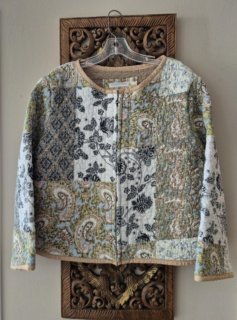 Pu&ograve; includere: Una giacca trapuntata con design patchwork e vari motivi nei toni del blu, verde, nero e bianco. Il capo presenta uno scollo rotondo, maniche lunghe e una chiusura frontale con zip, rifinito con un bordo color beige a tinta unita.