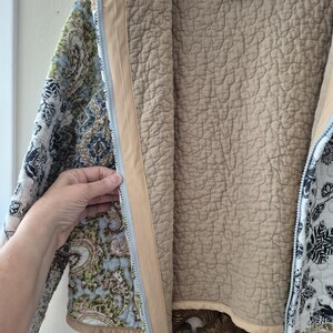 Pu&ograve; includere: Una giacca trapuntata con cerniera caratterizzata da un motivo floreale e paisley multicolore nei toni del blu, verde, nero e bianco. L'interno &egrave; foderato con tessuto beige tinta unita e include un'etichetta con la scritta Tenfel Creations.
