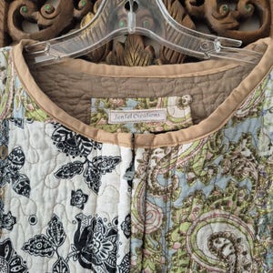 Pu&ograve; includere: Una giacca trapuntata caratterizzata da un mix di motivi floreali bianchi e neri insieme a stampe paisley azzurre, verdi e beige. Il capo presenta un bordo color beige attorno allo scollo e un'etichetta con scritto JenTel Creations.