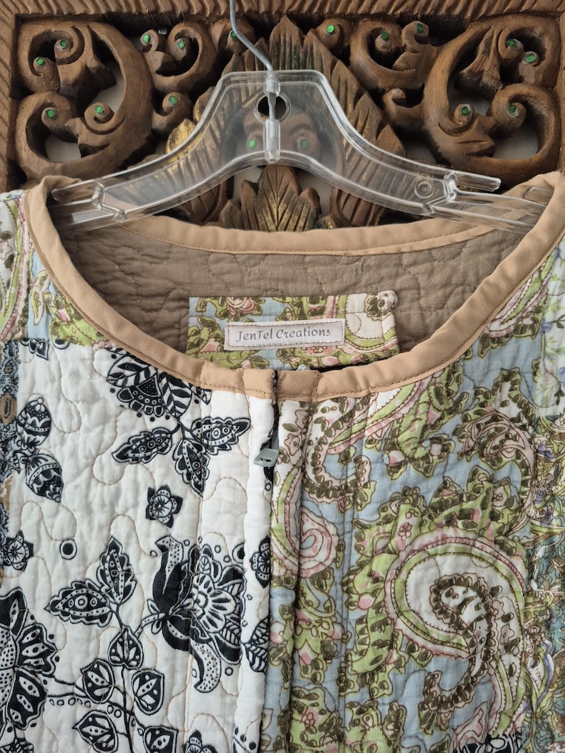 Pu&ograve; includere: Una giacca trapuntata caratterizzata da un mix di motivi floreali bianchi e neri insieme a stampe paisley azzurre, verdi e beige. Il capo presenta un bordo color beige attorno allo scollo e un'etichetta con scritto JenTel Creations.