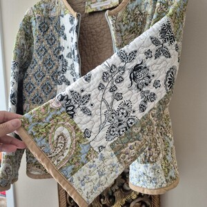 Pu&ograve; includere: Una giacca trapuntata con un design patchwork caratterizzato da vari motivi floreali e paisley nelle tonalit&agrave; del verde, blu, nero e bianco. La giacca presenta un bordo color cuoio lungo i profili, uno scollo rotondo e una fodera interna trapuntata color cuoio.