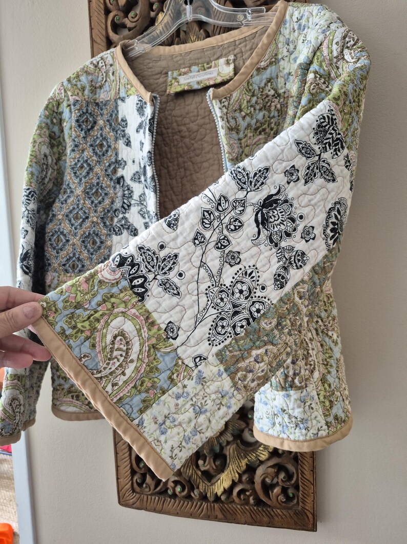 Pu&ograve; includere: Una giacca trapuntata con un design patchwork caratterizzato da vari motivi floreali e paisley nelle tonalit&agrave; del verde, blu, nero e bianco. La giacca presenta un bordo color cuoio lungo i profili, uno scollo rotondo e una fodera interna trapuntata color cuoio.