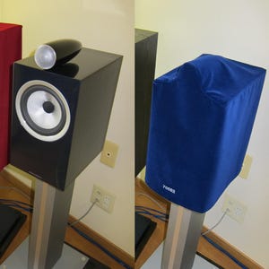 May include: A black speaker with a silver speaker grille and a blue speaker cover. The speaker is on a wooden stand with a grey base. The speaker cover has the text "70682" printed on it.