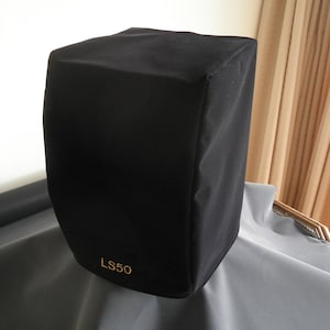 Puede incluir: Funda de altavoz negra con el texto "LS50" en letras doradas.