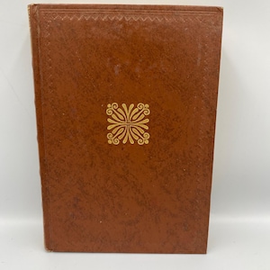 Könnte beinhalten: Ein braunes Hardcover-Buch mit einem goldenen Dekormuster auf dem Einband.