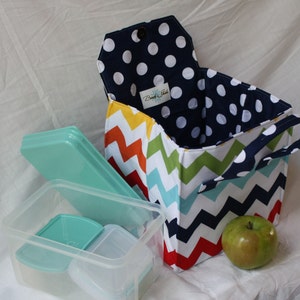 Peut inclure: Un sac &agrave; d&eacute;jeuner color&eacute; avec un motif en chevron et une doublure en pois bleu marine. Le sac a une poign&eacute;e et est ouvert pour r&eacute;v&eacute;ler un r&eacute;cipient &agrave; d&eacute;jeuner en plastique transparent avec un couvercle vert.
