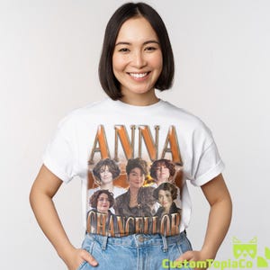 May include: White t-shirt featuring the name "ANNA" in large, orange, vintage-style lettering above a collage of six portraits. The name "CHANCELLOR" is printed below in a similar style.