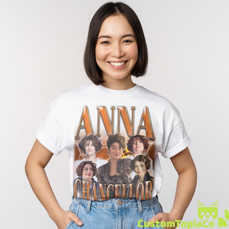 May include: White t-shirt featuring the name "ANNA" in large, orange, vintage-style lettering above a collage of six portraits. The name "CHANCELLOR" is printed below in a similar style.