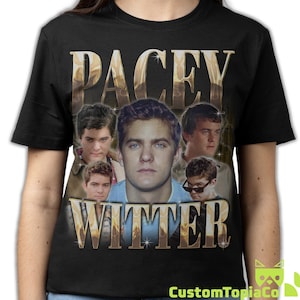 May include: A black short-sleeve t-shirt featuring a graphic print of Pacey Witter. The design includes the name PACEY WITTER in large gold lettering with a metallic effect, surrounding multiple photographic portraits of the character.