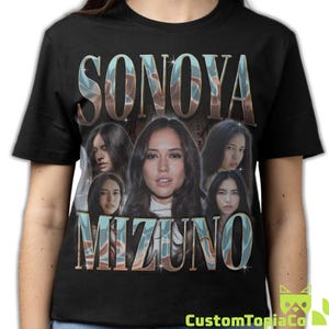 May include: A black short-sleeve t-shirt featuring a graphic print of Sonoya Mizuno. The design includes the text "SONOYA" at the top and "MIZUNO" at the bottom in a metallic blue and brown font, surrounding five different portraits of the actor.