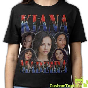 May include: Black t-shirt featuring the name "KIANA MADEIRA" in a vintage-style font with a red and blue gradient. The shirt includes multiple images of a woman. The CustomTopiaCo logo is in the bottom right corner.