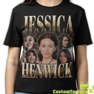 Può includere: T-shirt nero con il nome "JESSICA HENWICK" in un carattere dorato strutturato. La maglietta mostra più immagini di Jessica Henwick. Il logo CustomTopiaCo è visibile in basso a destra.