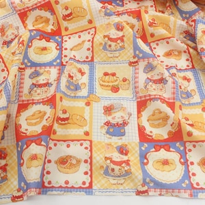 Puede incluir: Una tela con un patrón repetido de gatos de dibujos animados con trajes de chef, rodeados de productos horneados. Los cuadrados son rojos, amarillos y azules, con fondos blancos. La tela es probablemente de algodón o un material similar.