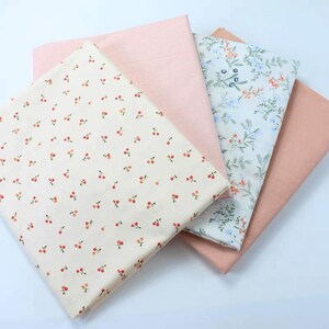May include: A selection of fabric swatches in different patterns and colours. One swatch has a cream background with a cherry print. Another has a pink striped design, and a third has a floral pattern with blue and orange accents. A solid peach-coloured fabric completes the set.