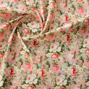 May include: Pink fabric with a floral pattern featuring white and pink roses. The fabric is folded and has a soft, delicate look.