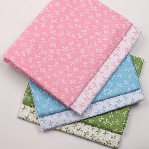 May include: A stack of five fabric squares with a white bow pattern on a pink, blue, white, green, and cream background.