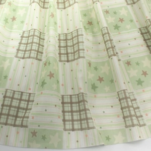 May include: Close-up of a fabric with a patchwork design. The fabric features alternating squares with a brown grid pattern and white stripes. The background is light green with star and dot patterns in various colours. The overall theme is a nursery or children's textile.