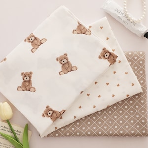 Peut inclure: Trois échantillons de tissu avec des motifs différents. L'échantillon du haut est blanc avec un motif d'ours en peluche brun. L'échantillon du milieu est blanc avec un motif de cœur brun. L'échantillon du bas est brun avec un motif de diamant blanc et des cœurs bruns.