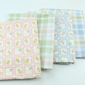 Peut inclure: Quatre morceaux de tissu pliés avec différents motifs. L'un présente un motif floral rose et jaune, un autre un motif à carreaux vert et blanc, un troisième avec des carrés floraux bleus et le dernier un motif à carreaux bleu et jaune.