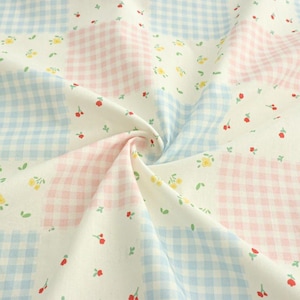 May include: Close-up of a fabric with a patchwork design. The fabric features squares of light blue and pink gingham, interspersed with white squares adorned with tiny yellow flowers and red berries. The fabric is slightly creased.
