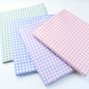 Peut inclure: Quatre morceaux de tissu à carreaux de différentes couleurs : vert, bleu, violet et rose. Le tissu est plié et empilé sur une surface blanche.