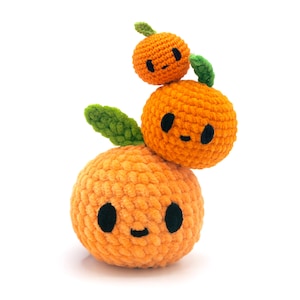 Op de afbeelding: Een stapel van drie gehaakte oranje bollen van verschillende groottes, elk met een klein groen blaadje bovenop en een eenvoudig zwart geborduurd gezichtje met twee ovale ogen en een klein mondje, gemaakt van zacht oranje garen.