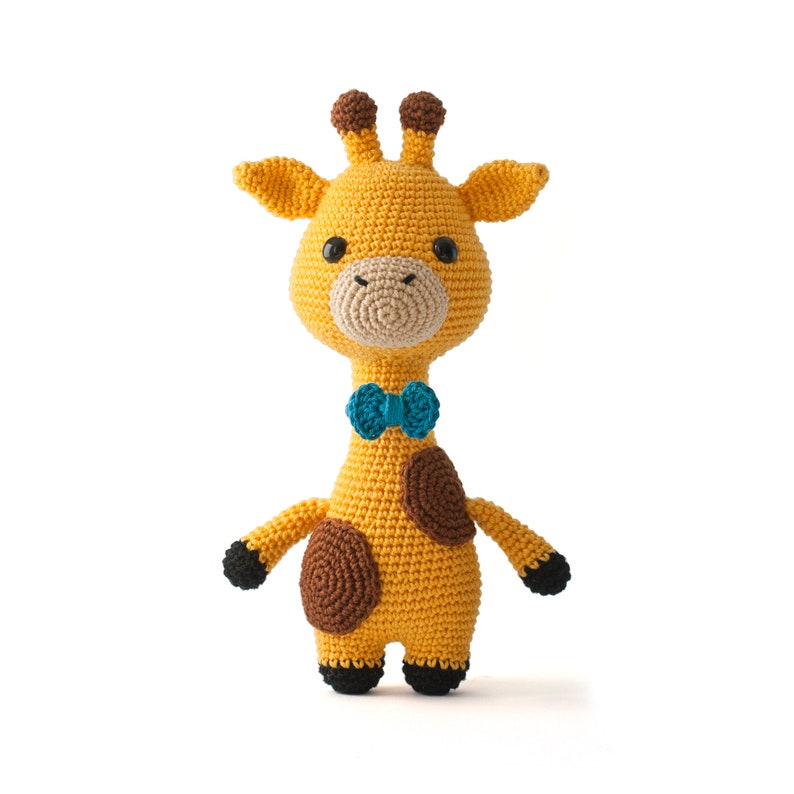 May include: A crocheted giraffe toy with brown spots, wearing a blue bow tie. The giraffe is yellow and has black eyes and a brown nose.
