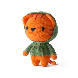 Pode incluir: Um bicho de pel&uacute;cia feito em croch&ecirc; com formato de tigre laranja com listras vermelho-escuras, olhos de pl&aacute;stico preto e nariz preto. O tigre veste um moletom com capuz verde-s&aacute;lvia com bolso frontal e cord&otilde;es combinando.