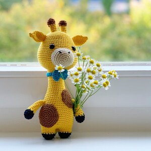 May include: A crocheted giraffe toy holding a bouquet of white daisies. The giraffe is yellow with brown spots and a blue bow tie.