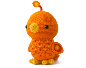 May include: A crocheted orange bird toy with yellow accents and black eyes. The bird has a small flower on its head and a circular pattern on its tail.