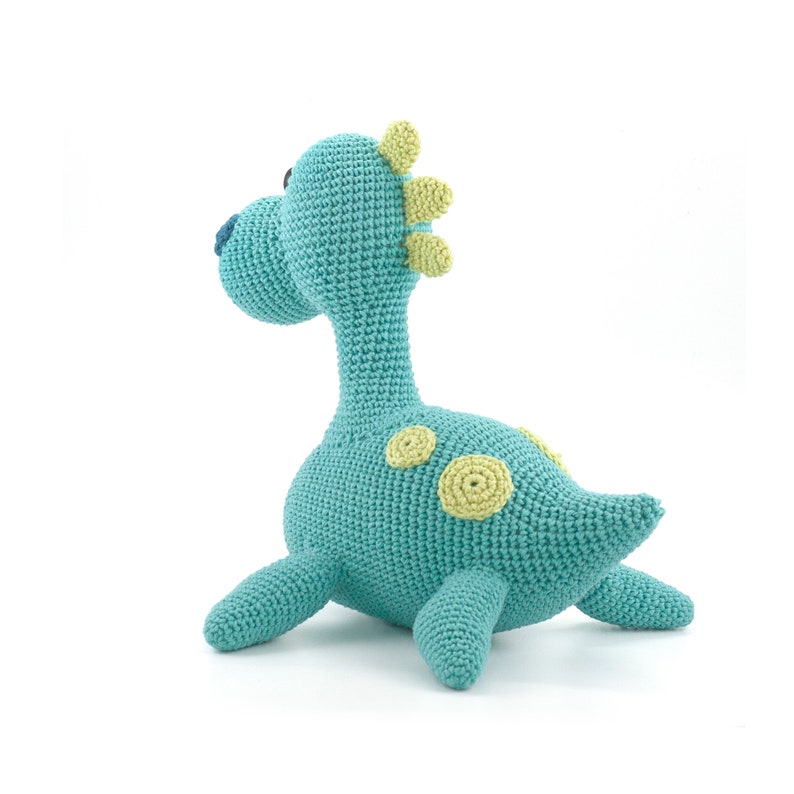 May include: A crocheted turquoise dinosaur toy with yellow accents. The dinosaur has a long neck, a small head, and a long tail. It has a few yellow spots on its body.