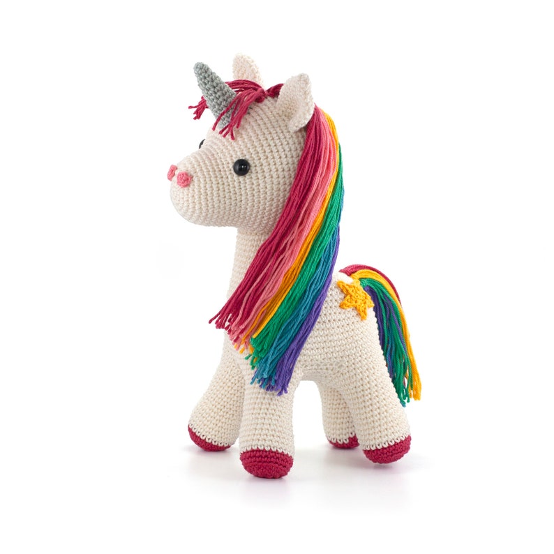 May include: A crocheted unicorn toy in cream, featuring a rainbow mane and tail. The unicorn has a gray horn, pink nose, and red hooves. A yellow star is stitched on its side. The toy is approximately 10 inches tall.