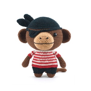 May include: A brown crocheted monkey wearing a black pirate hat with an eye patch, a red and white striped shirt, and black pants.