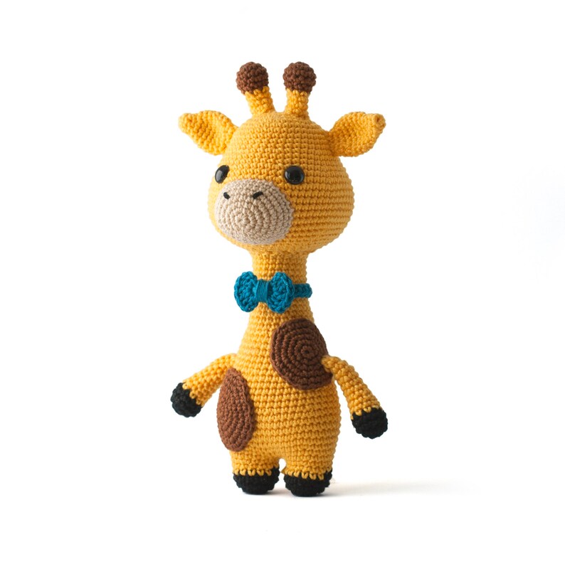 May include: A crocheted giraffe toy with brown spots, wearing a blue bow tie. The giraffe is yellow and has black feet.