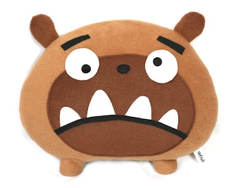 May include: Brown plush pillow with a cartoon monster face. The monster has big white eyes, a black nose, and a wide open mouth with white teeth. The pillow is labeled "Miffet!" in the bottom right corner.