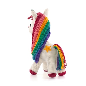May include: A crocheted unicorn toy with a white body, rainbow mane, and tail. The mane features pink, orange, yellow, green, blue, and purple yarn. A yellow star is sewn on the side. The hooves and the bottom of the legs are red.