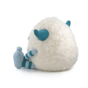 May include: A white crocheted plush toy with blue and white striped legs and blue horns. The toy is sitting on a white background.